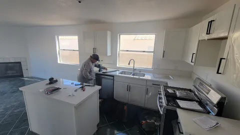 Active kitchen installation showing cabinets, island, sink, appliances and finish work in progress